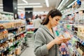 Young woman shopping in the supermarket grocery store.Reading ingredients,declaration or expiration date on a dairy product before