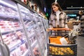 Young woman with shopping trolley chooses meat products at grocery supermarket. Royalty Free Stock Photo