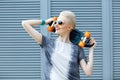 Young woman with short blonde hair smiling on the fashion background and holding little penny skateboard behind her head