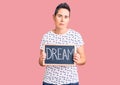 Young woman with short hair holding blackboard with dream word thinking attitude and sober expression looking self confident