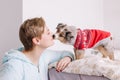 Young woman with short hair kissing cute puppy dog at home. Pet owner with a little furry friend. Small pet dog licking its owner