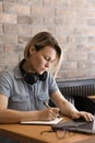 A young woman with short hair writes notes in a notebook and works on a laptop Royalty Free Stock Photo