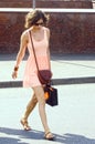 Young woman in a short pink dress summer, sunny day crossing the road near the restaurant Prague name