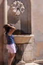 Young woman in shorts standing washes her hair at a drinking water fountain