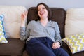 Young woman with shoulder-length dark hair is sprawled on the couch laughing and showing a victory hand gesture