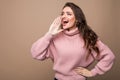 Young beauty woman shout and scream using her hands as tube, studio shoot isolated on brown