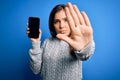 Young woman showing blank smartphone screen over blue isolated background with open hand doing stop sign with serious and Royalty Free Stock Photo