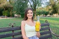 Young woman is showing a bottle of cool juice on the bench in the park Royalty Free Stock Photo