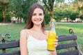 Young woman is showing a bottle of cool juice on the bench in the park Royalty Free Stock Photo