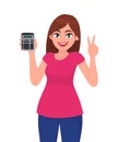 Young woman showing, holding calculator and making victory, peace or two sign. Trendy girl gesturing hand fingers.