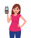 Young woman showing/holding pos payment terminal or credit/debit cards swiping machine while holding hand on hip. Royalty Free Stock Photo