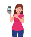 Young woman showing/holding pos payment terminal or credit/debit cards swiping machine and pointing finger. Wireless modern bank.