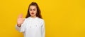 Young woman showing open hand doing stop sign with serious and confident expression, defense gesture. Indoor studio shot on yellow Royalty Free Stock Photo