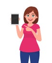 Young woman showing tablet and pointing hand towards that. Cute cheerful woman showing tablet computer with blank screen. Gadget.