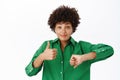 Young woman shows thumbs up and thumbs down with doubt, confused, making her choice, standing over white background Royalty Free Stock Photo