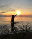 Young woman silhouette hand  up and trying touching sun down on  orange sunset at sea summer evening nature landscape Royalty Free Stock Photo