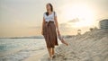Young woman with a silk scarf walking at sunset on a sandy sea beach. Happiness, travel, and holiday concepts Royalty Free Stock Photo