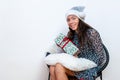Young woman in a silver santa hat sitting on a chair and holding a gift box in her hands, isolated on a white background Royalty Free Stock Photo