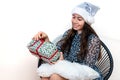 Young woman in a silver santa hat sitting on a chair and holding a gift box in her hands, isolated on a white background Royalty Free Stock Photo