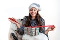 Young woman in a silver santa hat sitting on a chair and holding a gift box in her hands, isolated on a white background Royalty Free Stock Photo