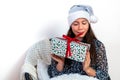 Young woman in a silver santa hat sitting on a chair and holding a gift box in her hands, isolated on a white background Royalty Free Stock Photo