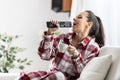 Young woman singing with a remote control while sitting on the couch, drinking coffee Royalty Free Stock Photo