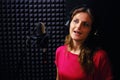 A young woman sings into a microphone on a black background. The singer performs the song at a professional recording Studio