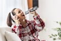 A young woman sings with a remote control and headphones on her ears while sitting on the couch Royalty Free Stock Photo