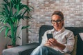 Young woman sit relax on sofa in living room browsing surfing wireless internet on smartphone, millennial girl rest on couch at Royalty Free Stock Photo