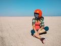 Young woman sits in the middle of desert wearing a helmet for buggy. Travel and sports concept