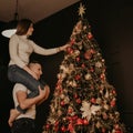 Young woman sits on back shoulders of man and decorates a Christmas tree Royalty Free Stock Photo