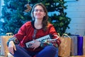 A young woman sits on the background of a Christmas tree with a musical instrument in her hands Royalty Free Stock Photo