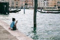 Young woman sits on the bank of Grand Canal browsing mobile phone.