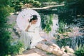 A young woman sits at a beautiful decorative lake, she is dressed in a tender Japanese kimono of ivory, a mint skirt