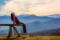 Young woman sits on bench outside and look at pictorial landscape with mountains