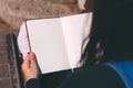 Young woman sits on bench in park with blank notebook and pen on her hands.