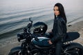 Young woman sits on motorbike on beach next coast of river