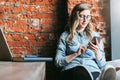 Young woman sits in cafe on windowsill and uses smartphone. Hipster girl checking e-mail, chatting, blogging, working. Royalty Free Stock Photo