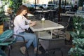 Young woman sits in chair at table in cozy street cafe