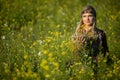 A young woman sits in a field of flowering rapeseed with a bouquet of herbs in her hand. Royalty Free Stock Photo