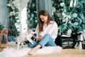 Woman sits near Christmas tree and plays with puppy of dalmatian dog