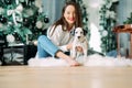 Woman sits near Christmas tree and plays with puppy of dalmatian dog