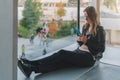 Woman sits on floor near window, uses smartphone.Hipster girl looking on screen of phone,blogging, browsing internet.