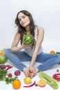 A young woman sits and holds a watermelon in her hands. Smiling brunette in jeans. Pile of vegetables and fruits on the floor. Royalty Free Stock Photo