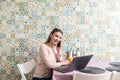 Young woman sits at the kitchen table using a laptop and talking on a cell phone Royalty Free Stock Photo