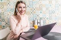 Young woman sits at the kitchen table using a laptop and talking on a cell phone Royalty Free Stock Photo