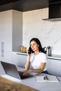 Young woman sits at the kitchen table using a laptop and talking on a phone Royalty Free Stock Photo