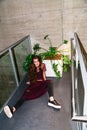 Young woman sits with legs spread next to plant