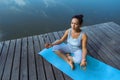 A young woman sits on a mat on a wooden pier in a lotus position with a rosary in her hands. View from above. Meditation, yoga in Royalty Free Stock Photo