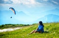 Young woman sits in the meadow and looks at the paraplane.